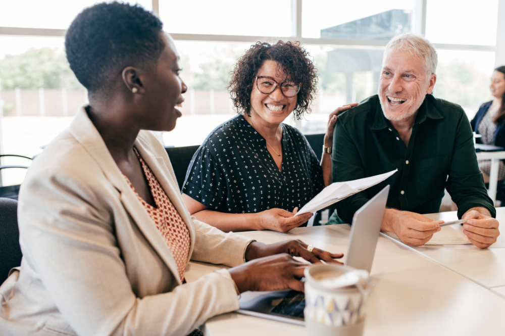 Three individuals engaged in early retirement planning, seated at a table with a laptop open before them.