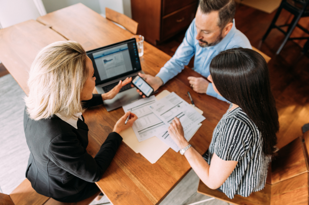 Three individuals collaborate at a table, reviewing paperwork to discuss the advantages of financial advisors.