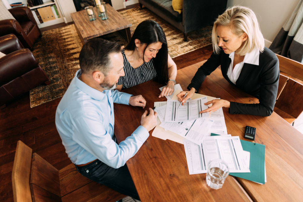 Three people, including a fiduciary financial advisor, sit at a table reviewing paperwork together.