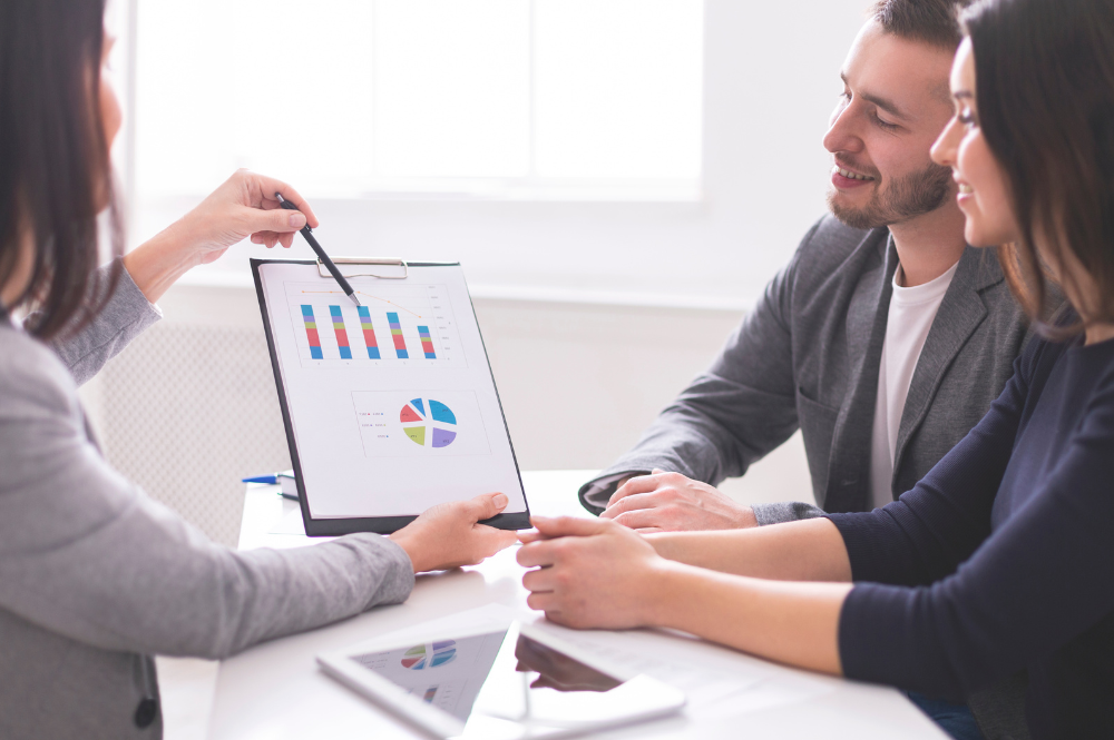 Three individuals discussing financial planning at a table with a tablet after a business sale.