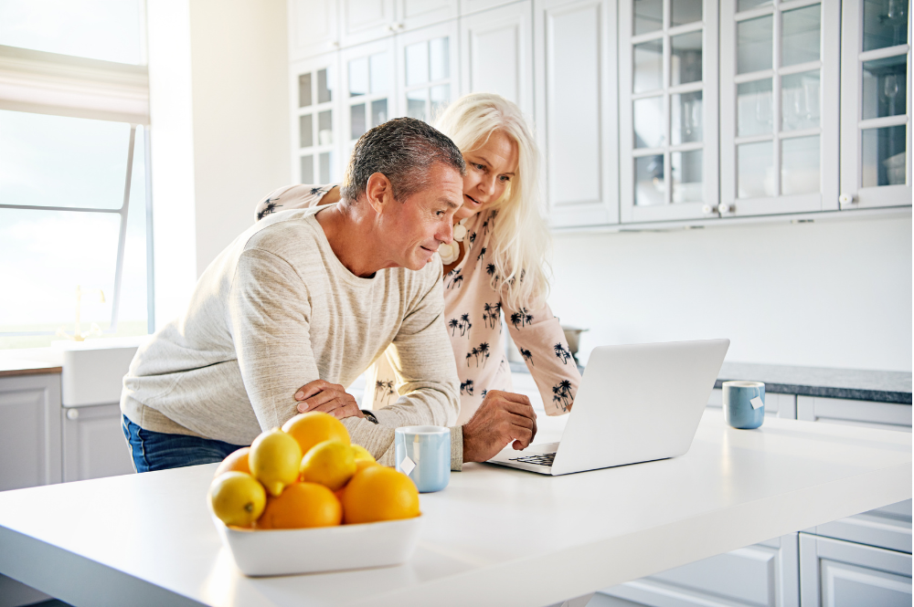 A man and woman examining a laptop screen in their kitchen, focused on retirement planning topics.