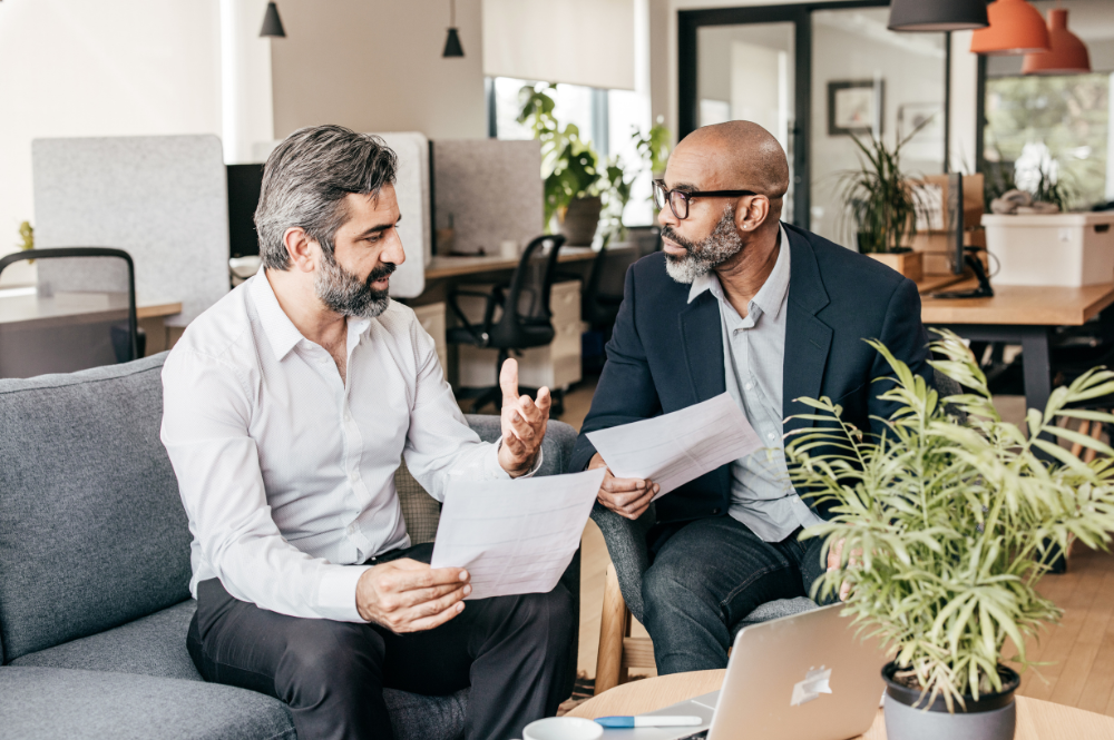 Two men discussing what is private wealth management while seated on a couch in a modern office setting.
