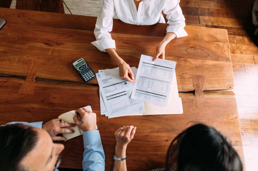 A group of three people at a table, analyzing documents and a calculator, contemplating the question of "do I need a wealth management advisor?